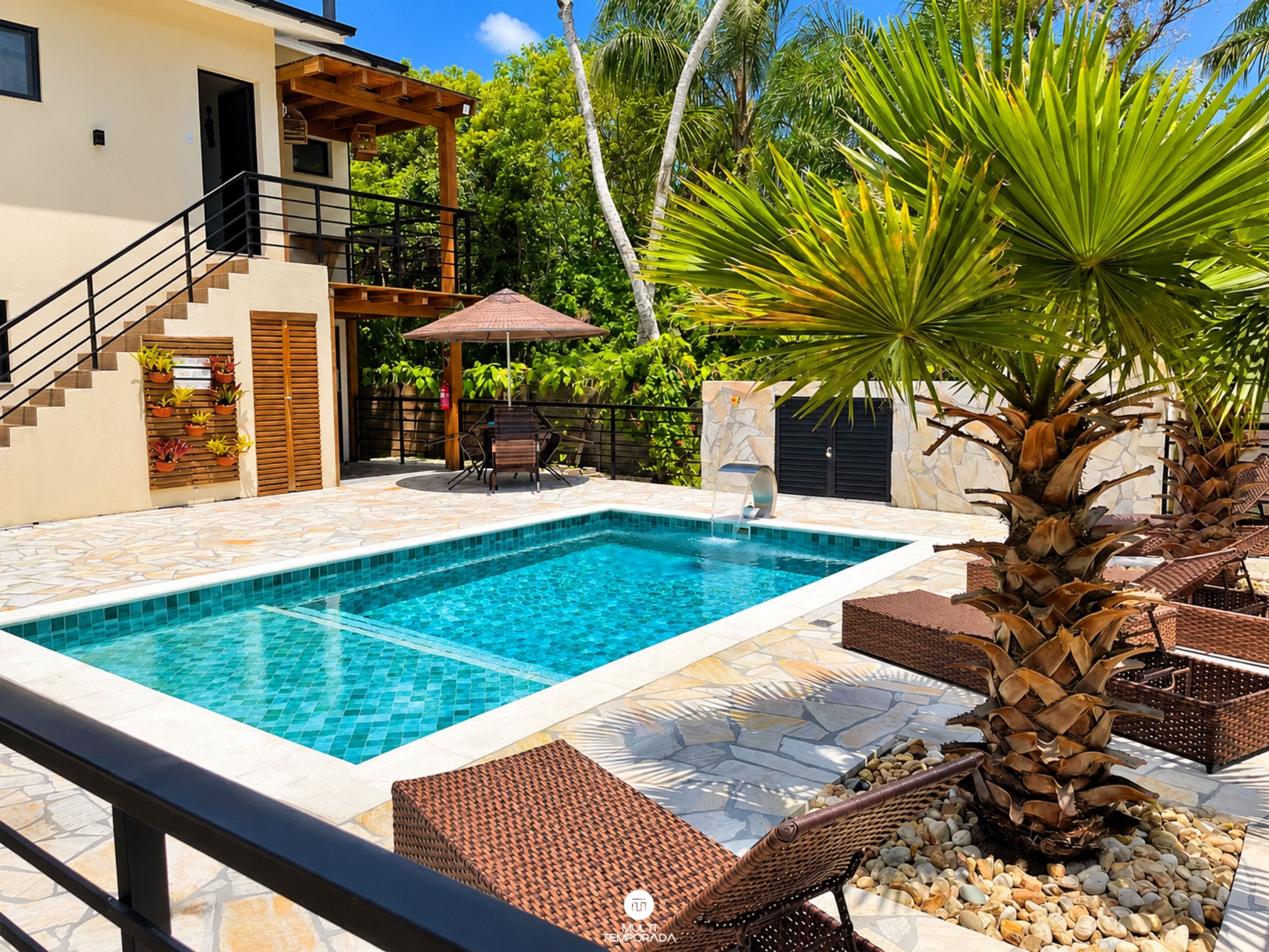 A swimming pool with a tiled deck, surrounded by lounge chairs and a palm tree.