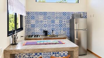 Una cocina con baldosas estampadas en azul y blanco, un refrigerador de acero inoxidable y una ventana con vistas a la vegetación.
