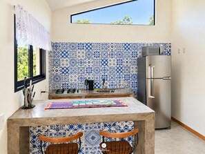 Une cuisine avec des carreaux bleus et blancs formant un motif, un réfrigérateur en acier inoxydable et une fenêtre donnant sur un paysage verdoyant.