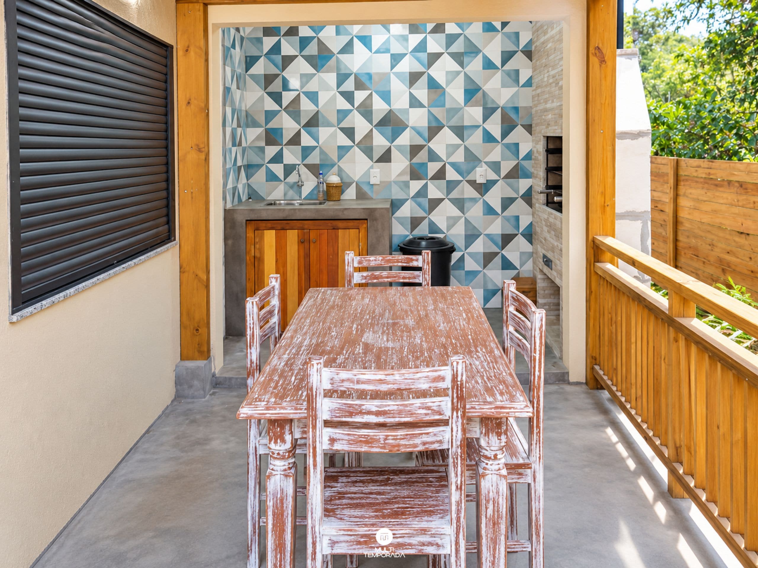 An outdoor patio with a wooden table and chairs, a tiled backsplash, and a wooden fence.