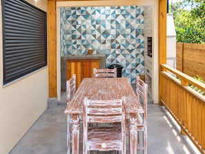 Une terrasse extérieure avec une table et des chaises en bois, un mur recouvert de carreaux et une clôture en bois.