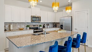 A modern kitchen with white cabinets, a granite countertop, stainless steel appliances, and blue bar stools. - Escape to a Themed Bedroom Retreat with PS5, Private Pool & BBQ (DAVENPORT)