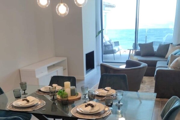 A dining area with a table set for four, a sofa, and a view of the ocean.