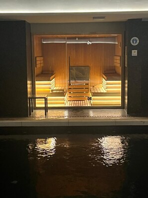 Uma sauna com bancos de madeira e porta de vidro, que dá acesso a uma área de piscina.