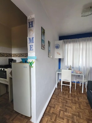 Una cocina compacta con refrigerador, una mesa de comedor con sillas y un cartel que dice 'Welcome'.