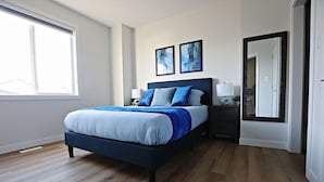 Un dormitorio con cama, mesitas de noche, espejo y cuadros en la pared.