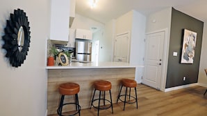 Una cocina moderna con gabinetes blancos, una estufa de acero inoxidable y una encimera con taburetes.