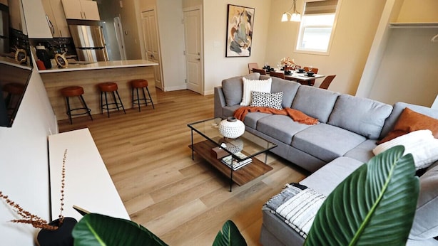 Una sala moderna con un sofá gris, una mesa de centro de vidrio y un área de comedor al fondo.