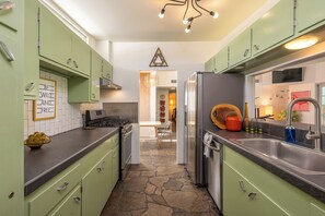 Una cocina con gabinetes verdes, un refrigerador de acero inoxidable y suelo de baldosas de piedra.