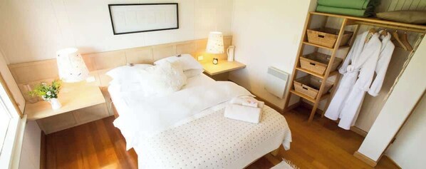 Habitación de hotel ordenada, con cama, mesitas de noche, lámpara, un cuadro enmarcado en la pared, armario de madera y toalla verde.