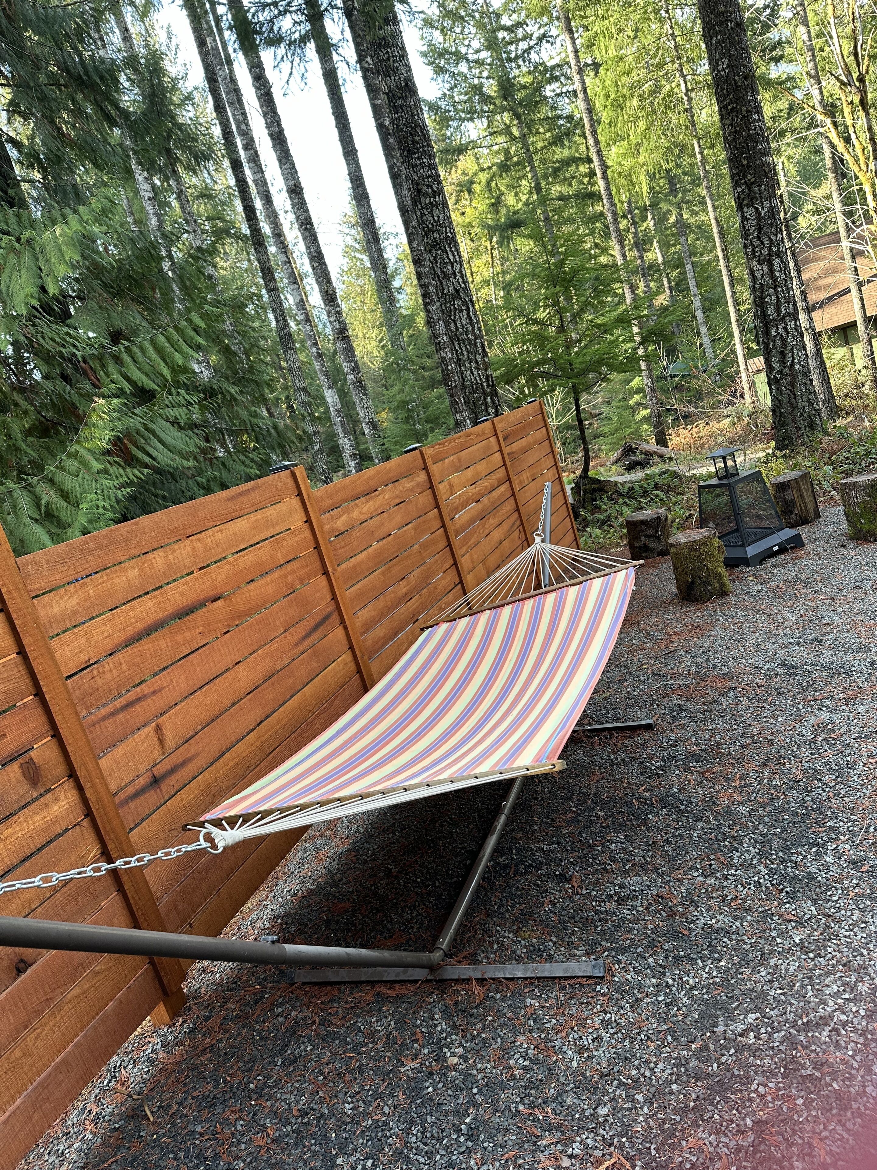 A hammock set up between wooden benches in a forested area with a gravel ground.