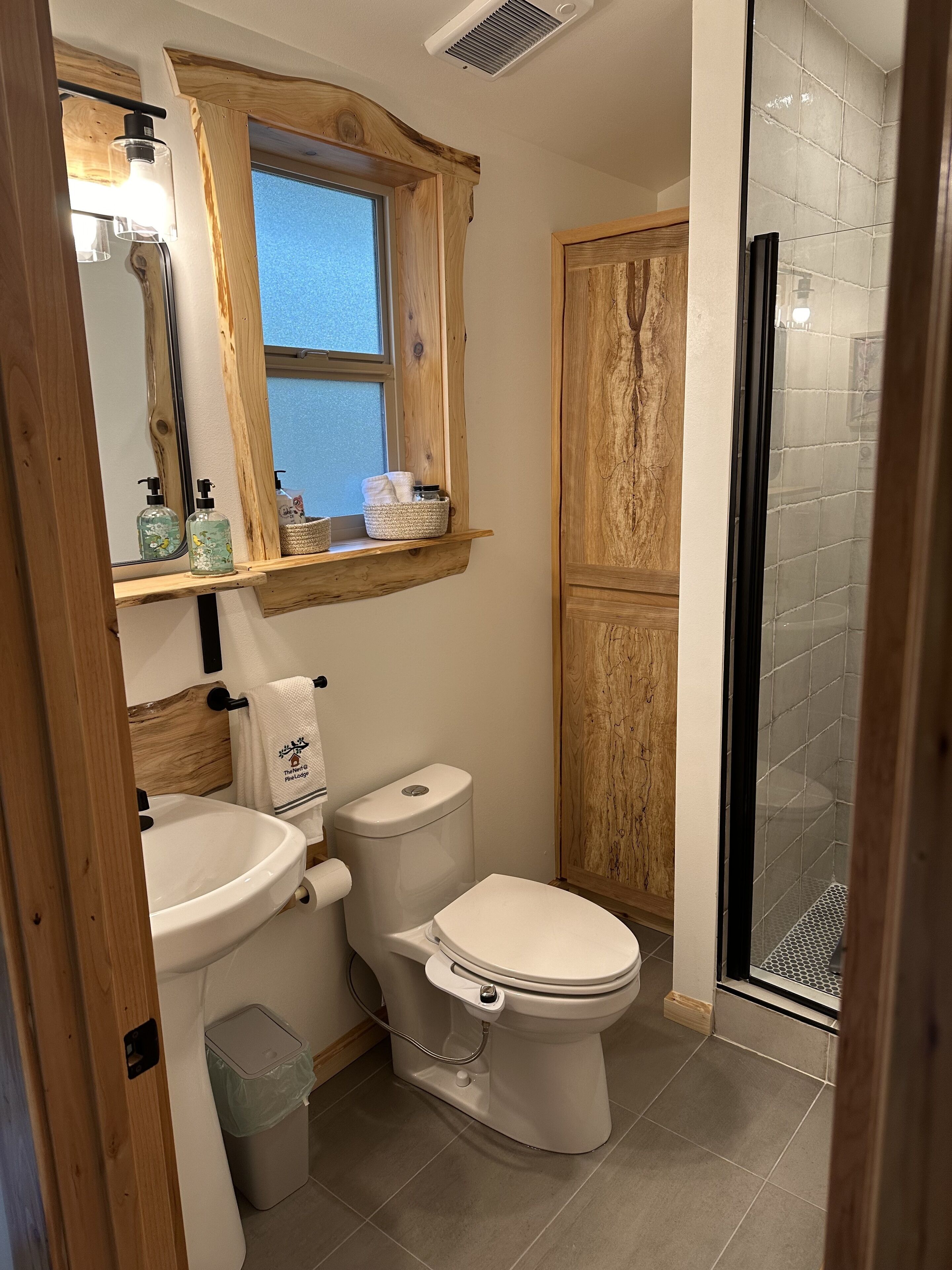 Un baño con tocador de madera, inodoro, lavamanos, ventana y zona de ducha.