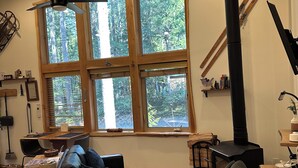 A cozy living room with a large window, a fireplace, and a ceiling fan.