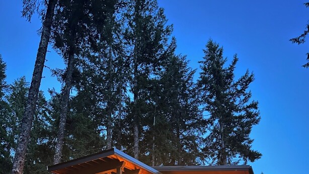 A wooden cabin with a covered porch, surrounded by trees.