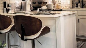 A kitchen with white cabinets, a central island with bar stools, a microwave, and a hanging light fixture. - Tiny Home | Grill, Near East Fork (Mentone)