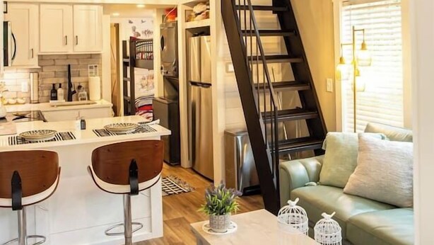 A modern kitchen with white cabinets, a central island, and a black staircase leading to an upper level. - Tiny Home | Grill, Near East Fork (Mentone)