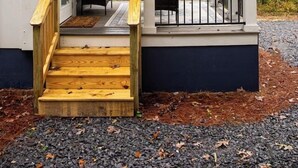 A covered porch with wooden steps leading to a seating area, surrounded by trees. - Tiny Home | Grill, Near East Fork (Mentone)