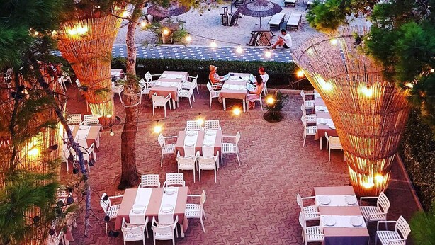 An outdoor dining area with tables and chairs, overlooking a beach and the sea. - Cosmo Beach Hotel (Durrës)