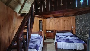 Una habitación rústica de madera con dos camas, un muro de piedra y una escalera de madera.