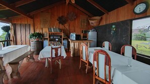 Un comedor rústico de madera con mesas y sillas, un reloj en la pared y vistas al exterior.