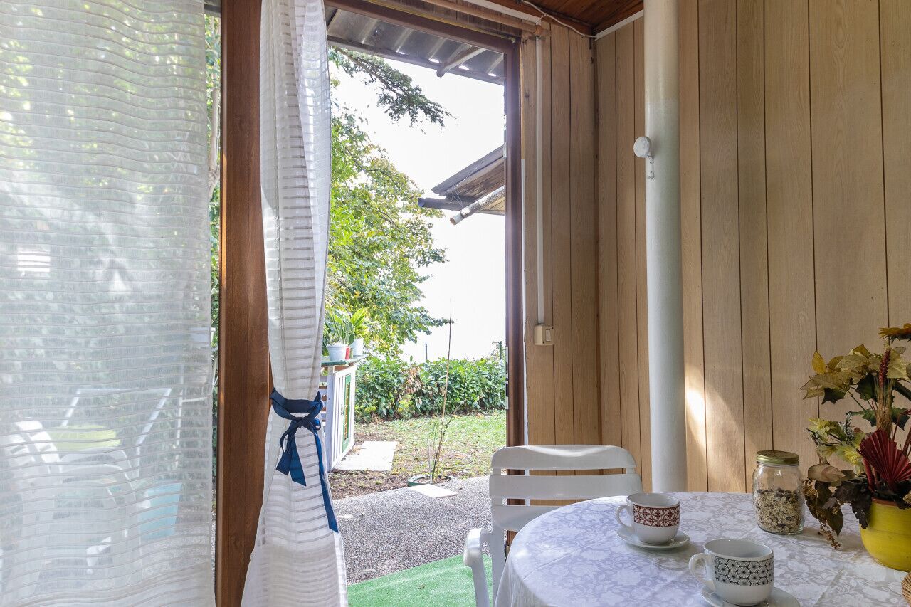 A room with a wooden door, a white chair, a table with a white tablecloth, and a vase with flowers.