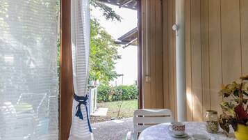 A room with a wooden door, a white chair, a table with a white tablecloth, and a vase with flowers.