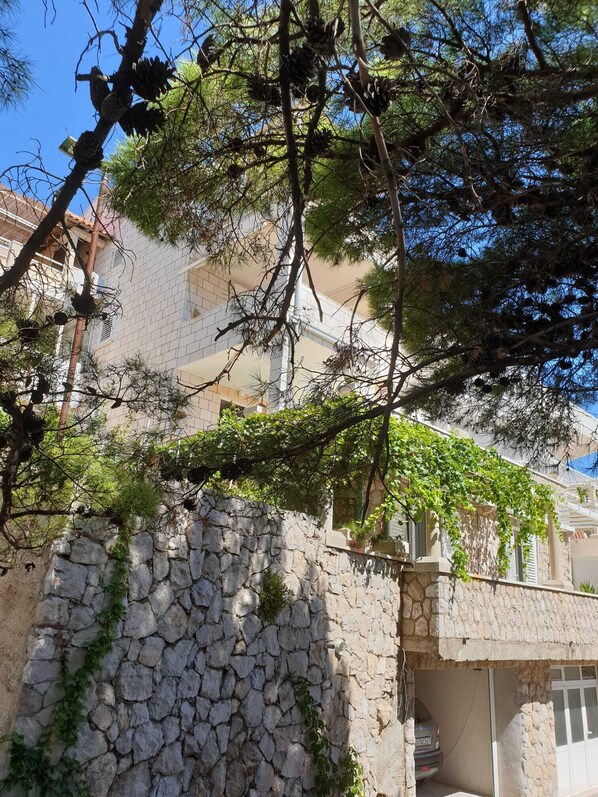 A stone wall with greenery, a building with balconies, and a clear blue sky.
