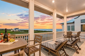 A balcony with a table set for two, a lounge chair, and a view of the ocean at sunset. - Private Beach Neighborhood | Pool | Sleeps 12 (Gilchrist)