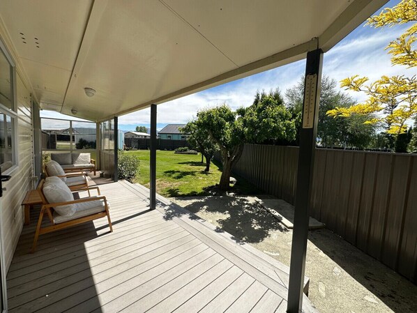 A covered patio with wooden flooring and a view of a backyard with a wooden fence and trees.