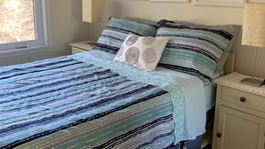 Une chambre à coucher avec une couvre-lit à rayures, une table de chevet avec une lampe et des tableaux encadrés accrochés au mur.