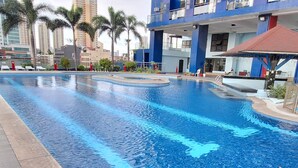 A swimming pool with clear blue water, surrounded by palm trees and modern buildings. - Manila Bayview Rental Luxury 3BR 3BA Condo w/Balcony Sunset View Pool Kitchen (Manila)