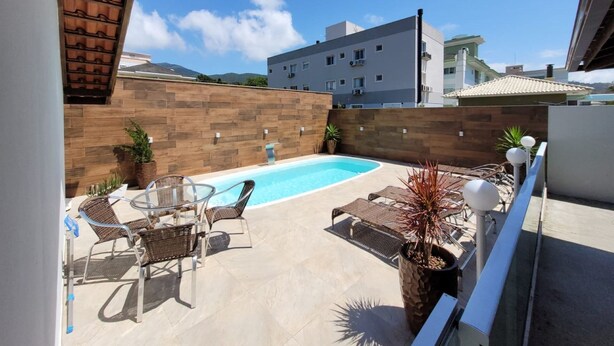 A rooftop pool area with a clear blue pool, wicker lounge chairs, and a pergola structure.