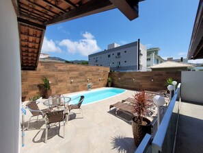 Uma área de piscina no terraço com piscina azul cristalina, cadeiras de espreguiçadeira de vime e uma estrutura de pérgula.