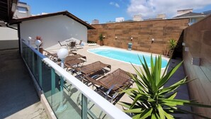 A rooftop pool area with lounge chairs and a glass balustrade.