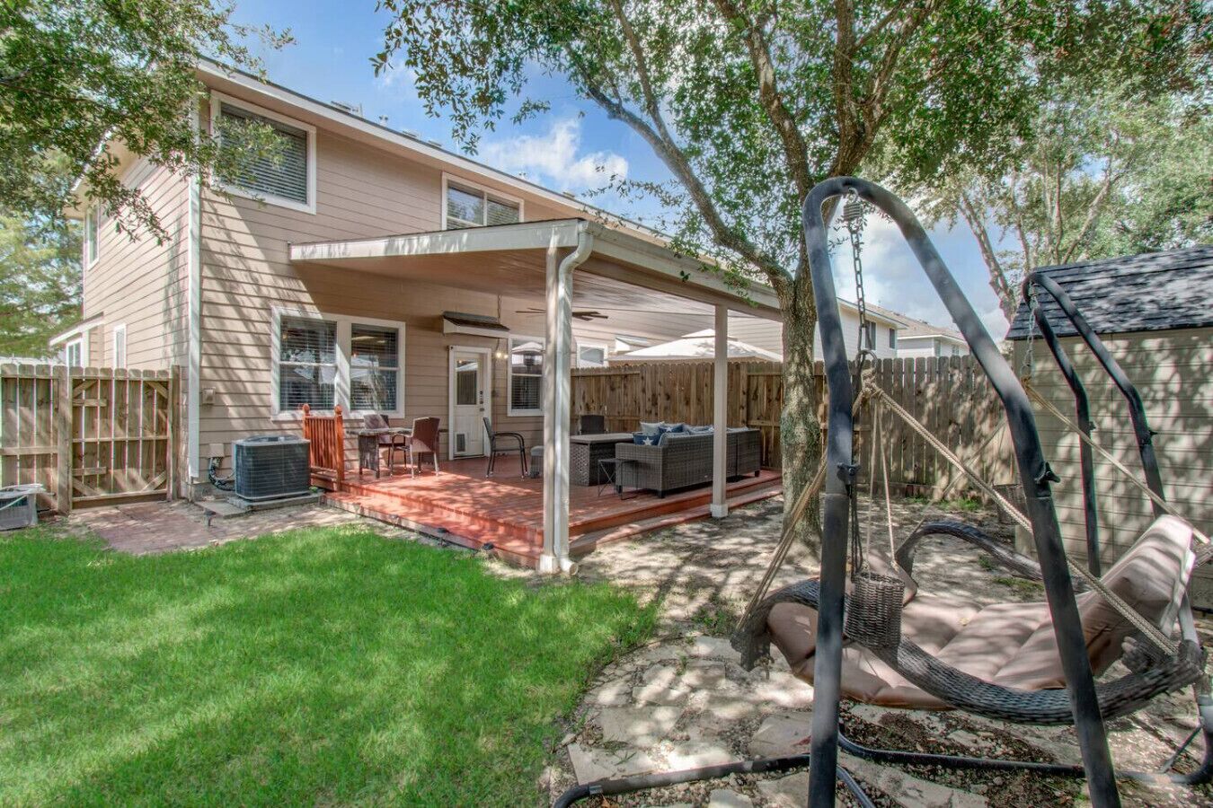 A covered patio area with outdoor furniture, a swing set, and a wooden fence.