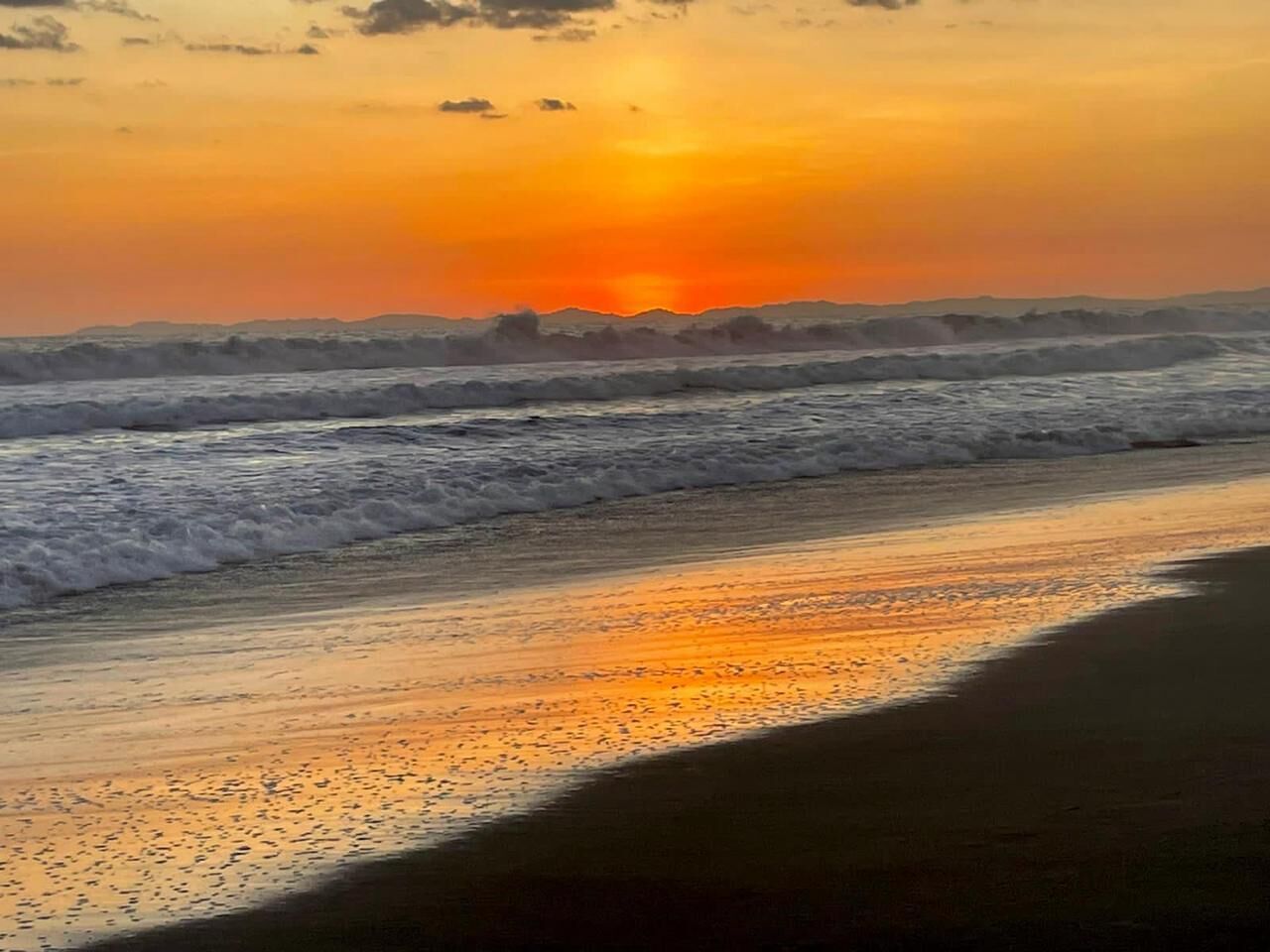A beach at sunset with waves and a clear sky.
