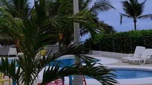 A pool area with a lamp post, palm trees, and lounge chairs. - Spectacular beachfront apartment, Spacious terrace with an unparalleled view. (Palo Grande)