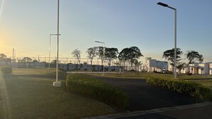 Un parking entouré d’une clôture, avec des lampadaires et une rangée de bâtiments blancs.