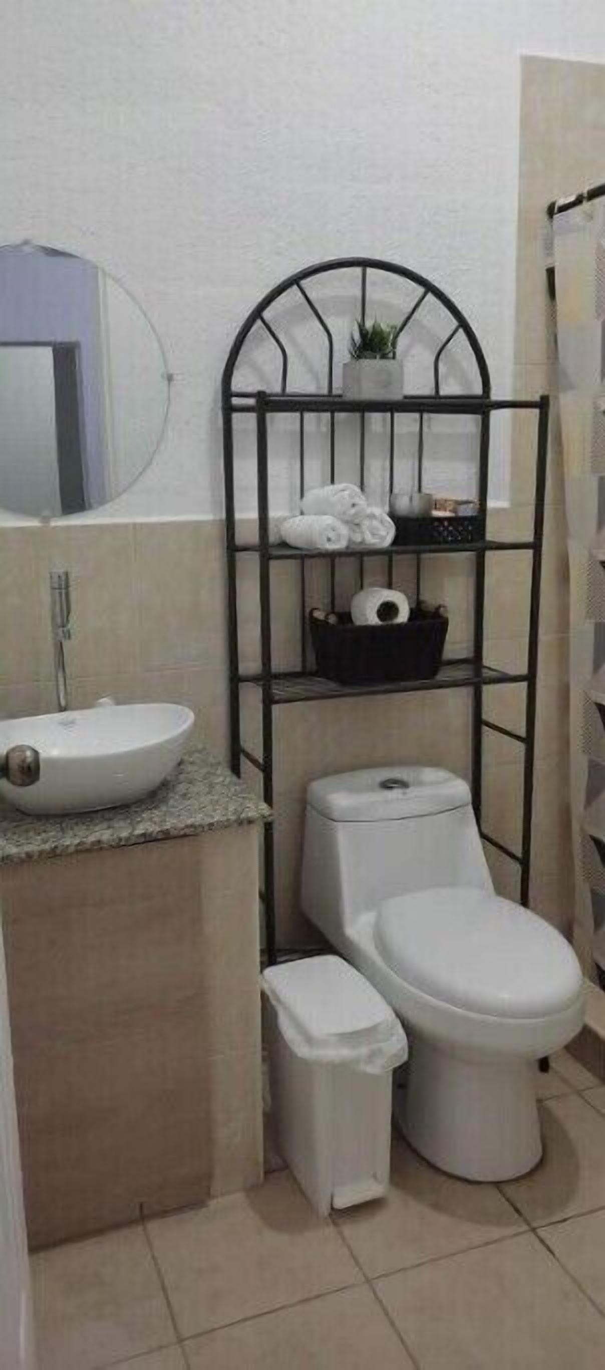 A compact bathroom with a white sink, toilet, and bidet, a metal shelf with towels, and a mirror.