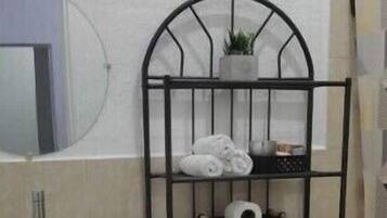 A compact bathroom with a white sink, toilet, and bidet, a metal shelf with towels, and a mirror.