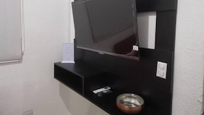 Un meuble noir pour télévision à écran plat, une petite plante en pot et un bol métallique.