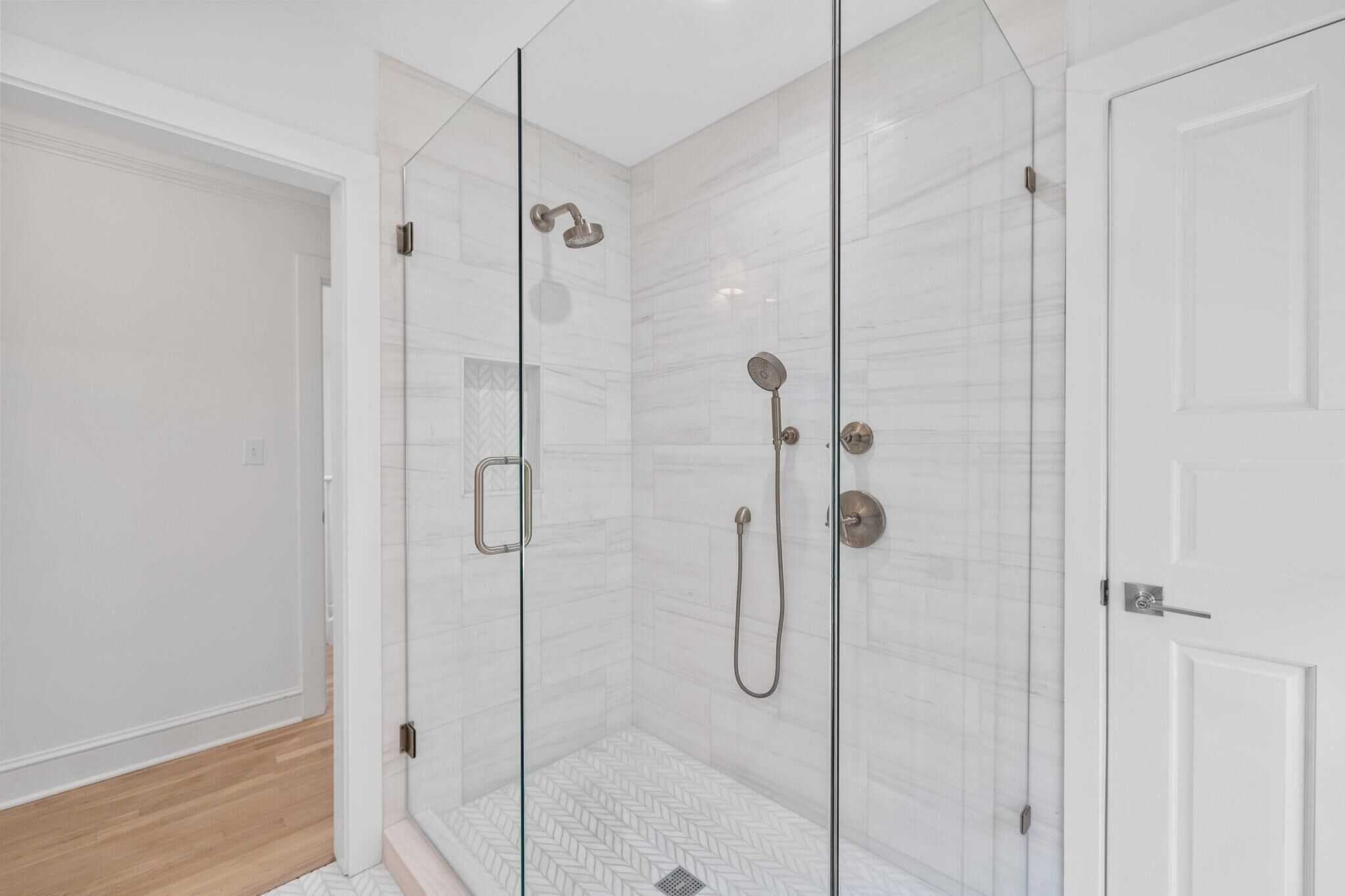 Een moderne badkamer met een douchecabine van glas, witte betegelde wanden en een houten vloer.