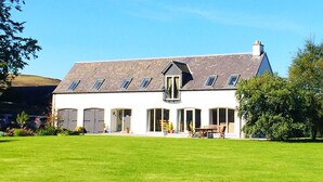 Une maison à deux étages, avec un toit en pente, de nombreuses fenêtres et un porche à l’avant.