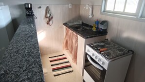 A compact kitchen with a granite countertop, a gas stove, and a built-in oven. - Jardim das Orquídeas 1 (Rio das Ostras)