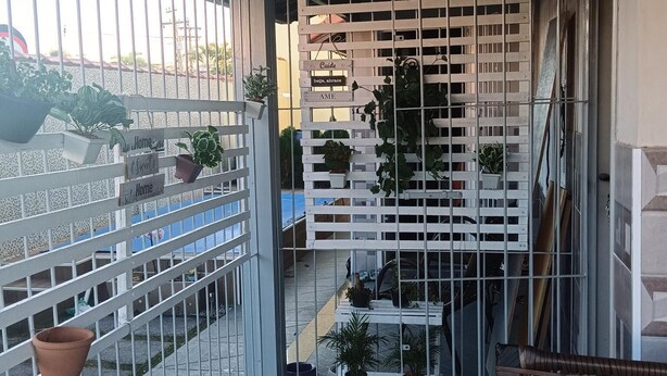 A covered outdoor area with a metal fence, potted plants, and a bench. - Jardim das Orquídeas 1 (Rio das Ostras)