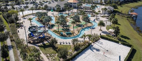 An aerial view of a resort with a central swimming pool, multiple water slides, and a sandy beach area.