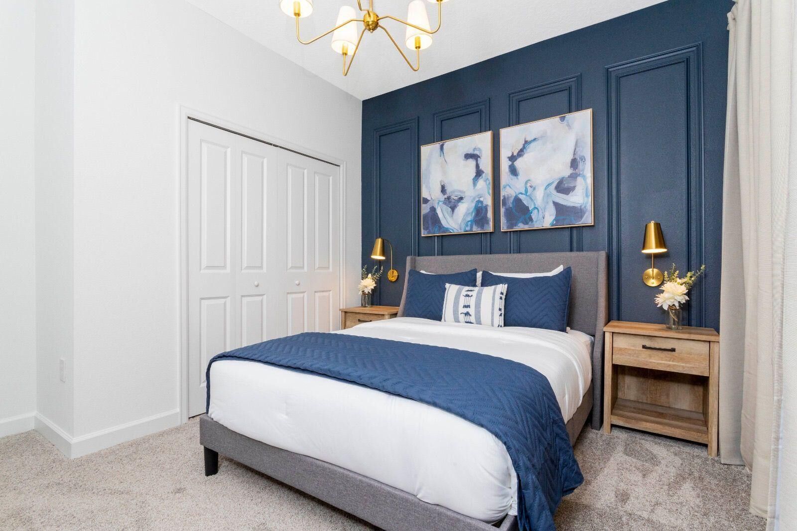 A bedroom with a bed, two nightstands, a chandelier, and artwork on the wall.