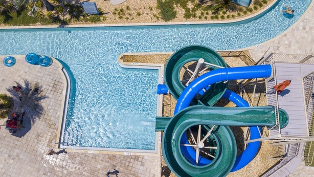 An aerial view of a swimming pool with two large water slides, a tiled deck area, and a few people around the pool. - 2994 - Great Family Home near Disney, private pool, Storey Lake Resort (Kissimmee)
