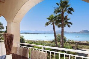 Un balcon avec vue sur une mer calme, un palmier et des montagnes à l’horizon.