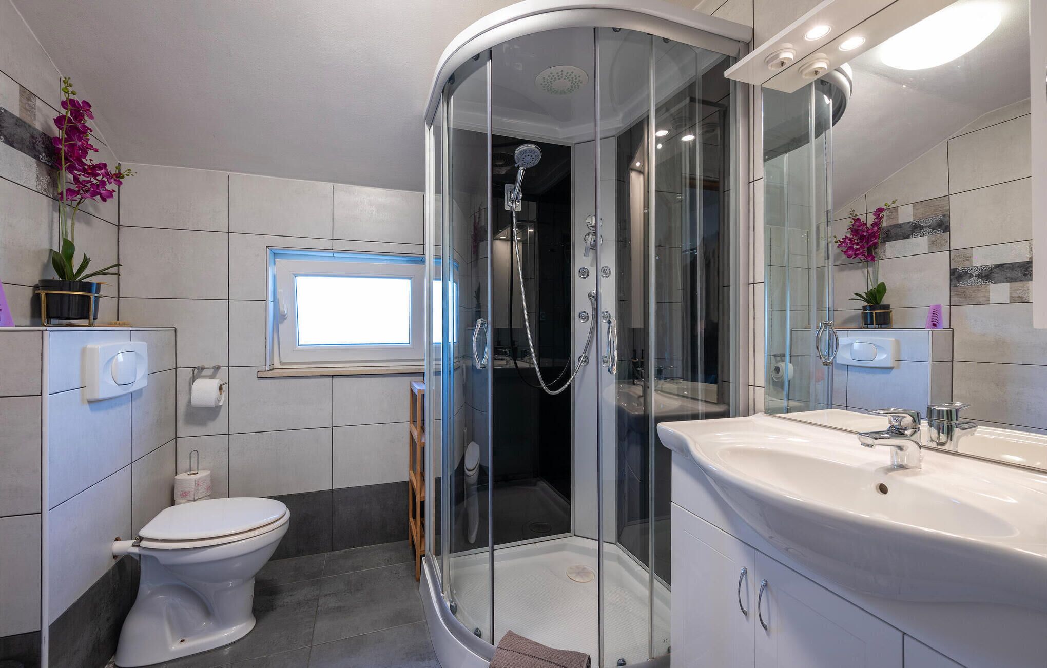 A modern bathroom with a glass-enclosed shower, a toilet, a sink, and a window.